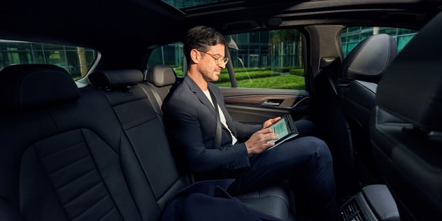 A man uses a tablet from the backseat of a BMW 