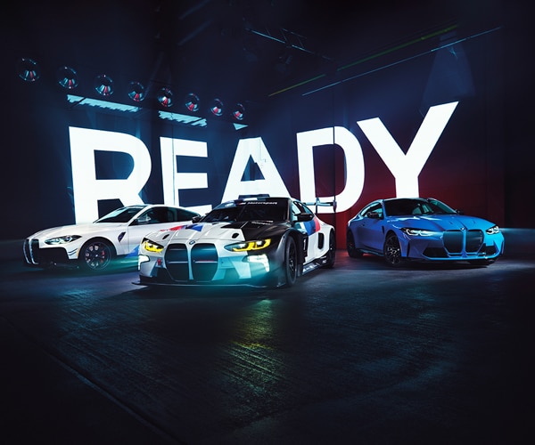 BMW M2 and M4 GT3 race cars parked in front of a screen reading READY
