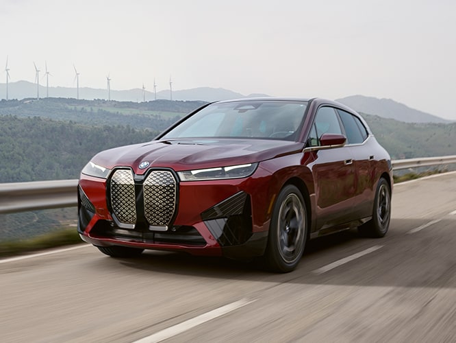 The BMW iX xDrive driving down an open road with wind turbines in the background