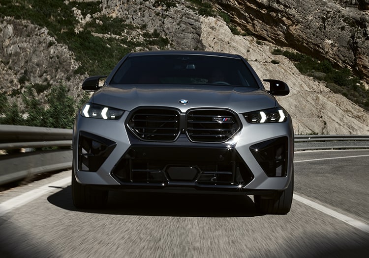 Front view of the 2026 BMW X6 M driving down a rural highway