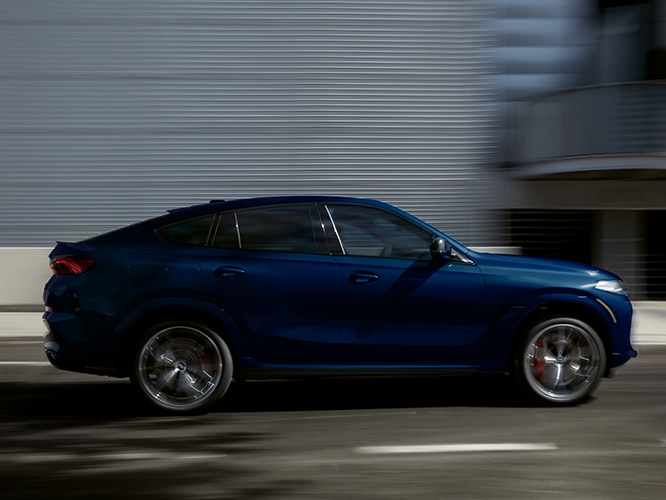 Exterior side view of the 2026 BMW X6 M60i in motion on a city street
